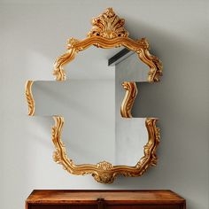 an ornate gold framed mirror hangs on the wall next to a wooden dresser with drawers