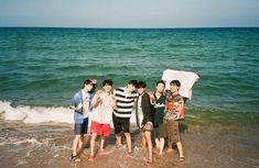 four young men standing in the ocean with an umbrella