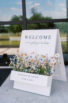 a welcome sign sitting on top of a table next to a window with flowers in it