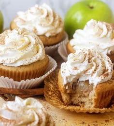 several cupcakes with frosting and cinnamon on top sitting next to an apple