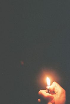 a person holding a small lit candle in their left hand, against a dark background