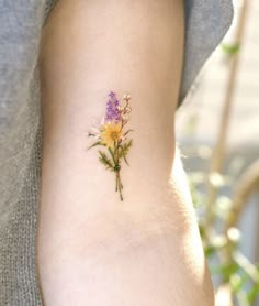 a small flower tattoo on the right side of the arm, with yellow and purple flowers