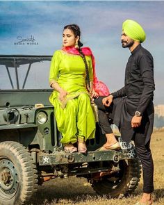 a man and woman sitting on the back of a green jeep in an open field