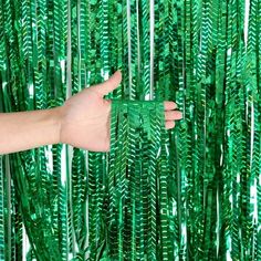 a person's hand is reaching up towards a green wall made out of palm leaves