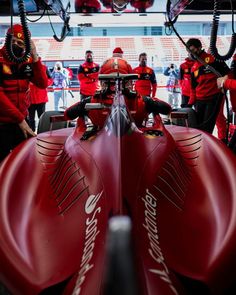 the front end of a racing car with some men in red uniforms standing around it