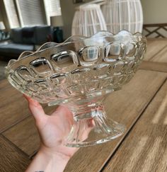 a hand holding a glass bowl on top of a wooden table