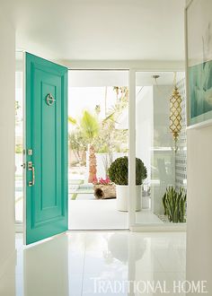 an open door leading to a patio with potted plants on the floor and palm trees in the background