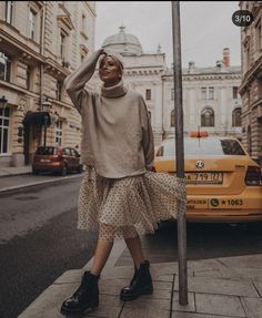 a woman is standing on the sidewalk next to a street sign wearing a sweater and polka dot skirt