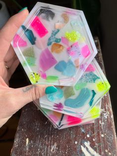 a person holding up some colorful soap on top of a wooden table