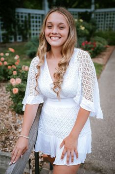 a young woman posing for a photo in front of some flowers and bushes with her hands on the railing