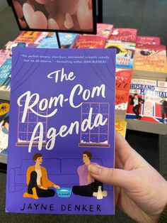 a person holding up a book about the rom - com agenda in front of bookshelves