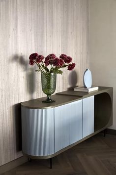 a vase filled with flowers sitting on top of a wooden table next to a wall