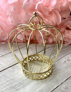 a small gold metal birdcage on a wooden table with pink flowers in the background