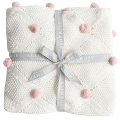 a white blanket with pink pom - poms on it and a ribbon around the edge