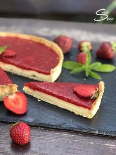 two slices of strawberry cheesecake on a slate board with fresh strawberries around it