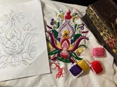 two different types of embroidery are on the table next to an open book and some scissors