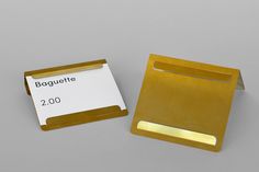 a gold business card holder next to a white paper with the name baguette on it