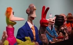 several puppets wearing suits and ties are lined up in a row, with one man holding his hand out to the other