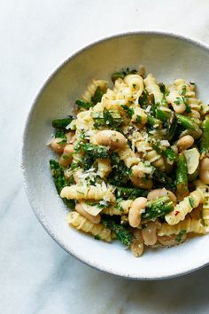 a white bowl filled with pasta and broccoli on top of a marble counter