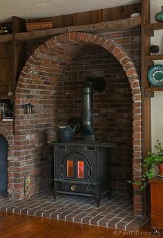 an old fashioned stove in the corner of a living room with brick walls and wood floors