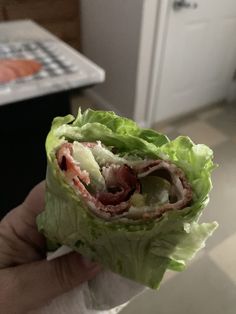 a hand holding up a lettuce wrap with meat and cheese on it in front of a kitchen counter