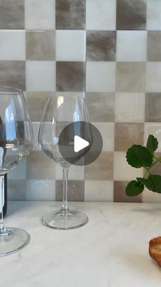 two wine glasses sitting on top of a counter next to a piece of bread and a plant