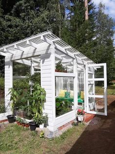 a small white house sitting in the middle of a yard with potted plants inside