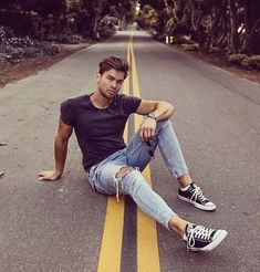 a young man sitting on the side of an empty road