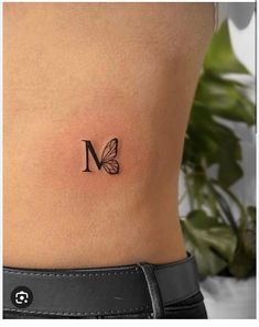 a small butterfly tattoo on the side of a woman's stomach, with the letter m behind it