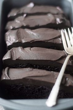 a fork sitting on top of a piece of cake in a pan with chocolate frosting