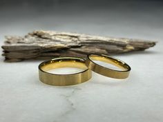 two gold wedding rings sitting next to each other on a piece of drifty wood