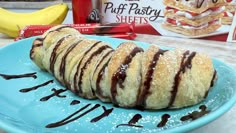 a blue plate topped with chocolate covered pastry next to a box of puff pastry sheets