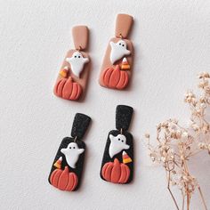 three halloween themed earrings with ghost, penguin and pumpkins on them next to some dried flowers