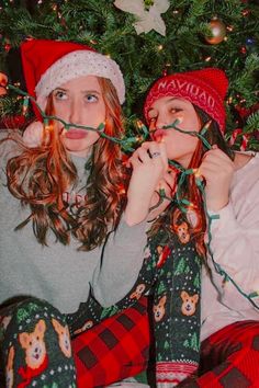 two young women sitting next to each other in front of a christmas tree with lights