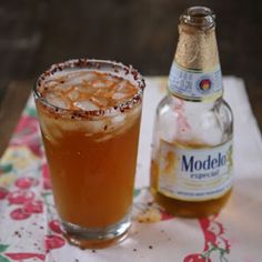 a bottle and a glass filled with liquid on top of a floral table cloth next to a drink