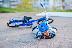 a young boy laying on the ground next to a blue tricycle with a helmet on