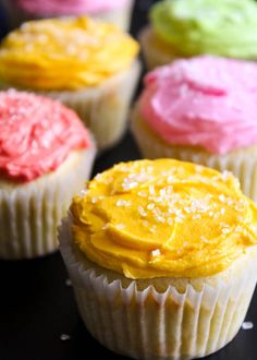 cupcakes with different colored frosting sitting on a black counter top in rows