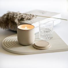 a candle sitting on top of a white table next to a book and glass cup