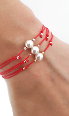 a close up of a person wearing red string bracelets with pearls and beads on them