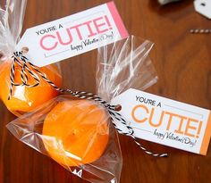 two oranges wrapped in plastic sitting on top of a wooden table next to a sign that says, you're cute