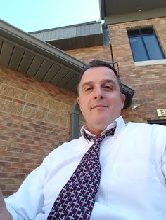 a man wearing a white shirt and tie standing in front of a brown brick building