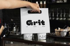 a person holding up a white bag with the word grit on it in front of a counter