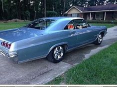 an old blue car parked on the side of a road in front of a house