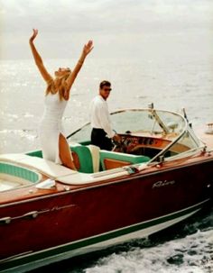 a man and woman riding on the back of a boat with their arms in the air