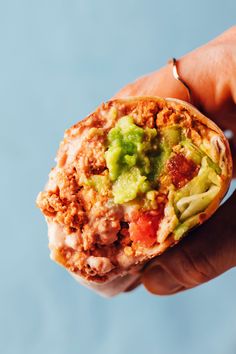 a hand holding a burrito filled with meat and veggies on top of it