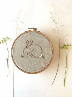 a cross stitch bunny rabbit sitting on the ground in front of some flowers and grass