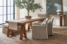 a wooden table sitting in the middle of a room next to two chairs and a potted plant