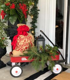 a red wagon filled with christmas decorations on the front porch next to potted plants