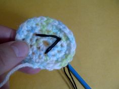 a crocheted object being held by someone's hand with a blue knitting needle