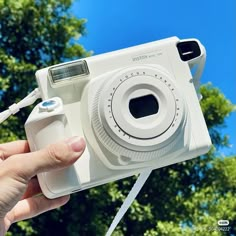 a person holding up a white camera in front of trees